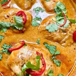 A dish full of chicken thighs in a red Thai sauce